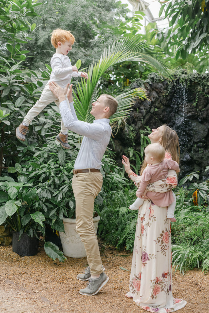 Mom holding little girl while dad throw little boy into the air 
