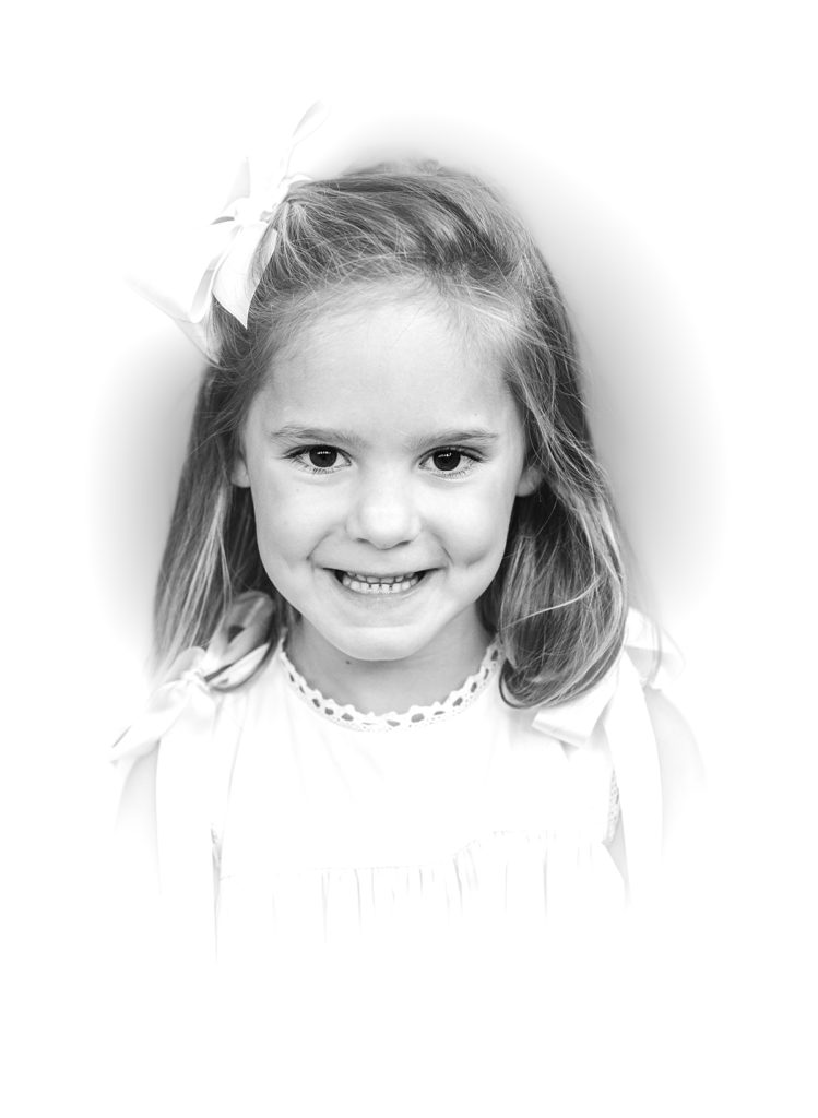 Black and White Heirloom Portrait little girl wearing a white dress with ecru ribbon smiling at the camera