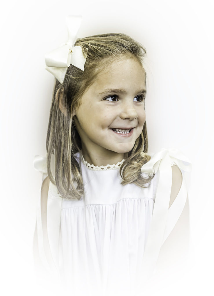 Black and White Heirloom Portrait little girl wearing a white dress with ecru ribbon smiling over her shoulder into the distance