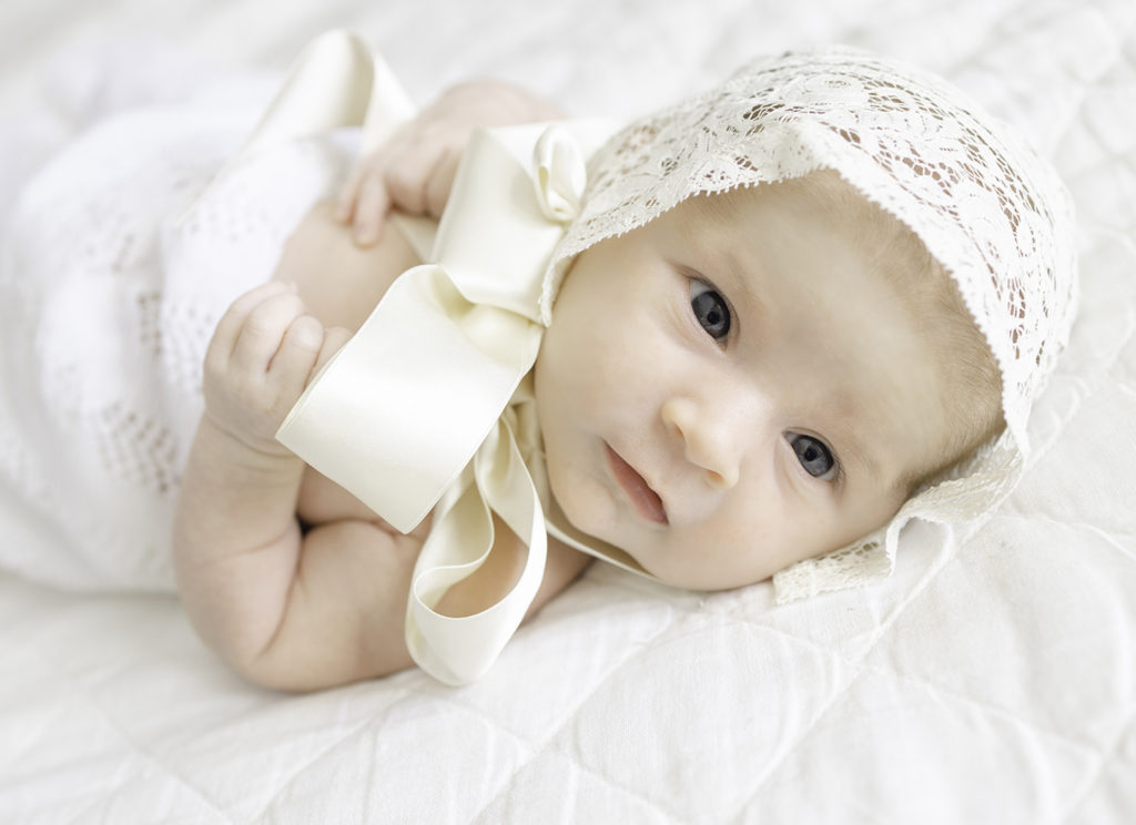 Newborn baby in lace bonnet wrapped in swaddle on bed by Birmingham Newborn Photographer Whitney Carr Photography 