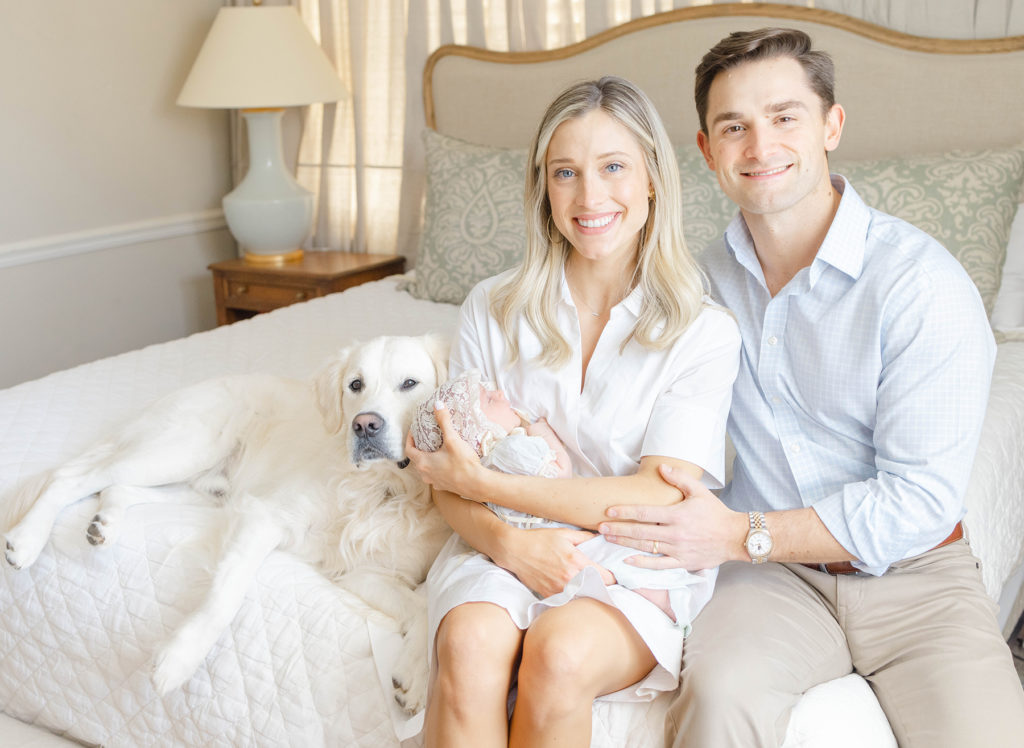Parents holding newborn baby with dog sitting on their bed by Birmingham Newborn Photographer Whitney Carr Photography