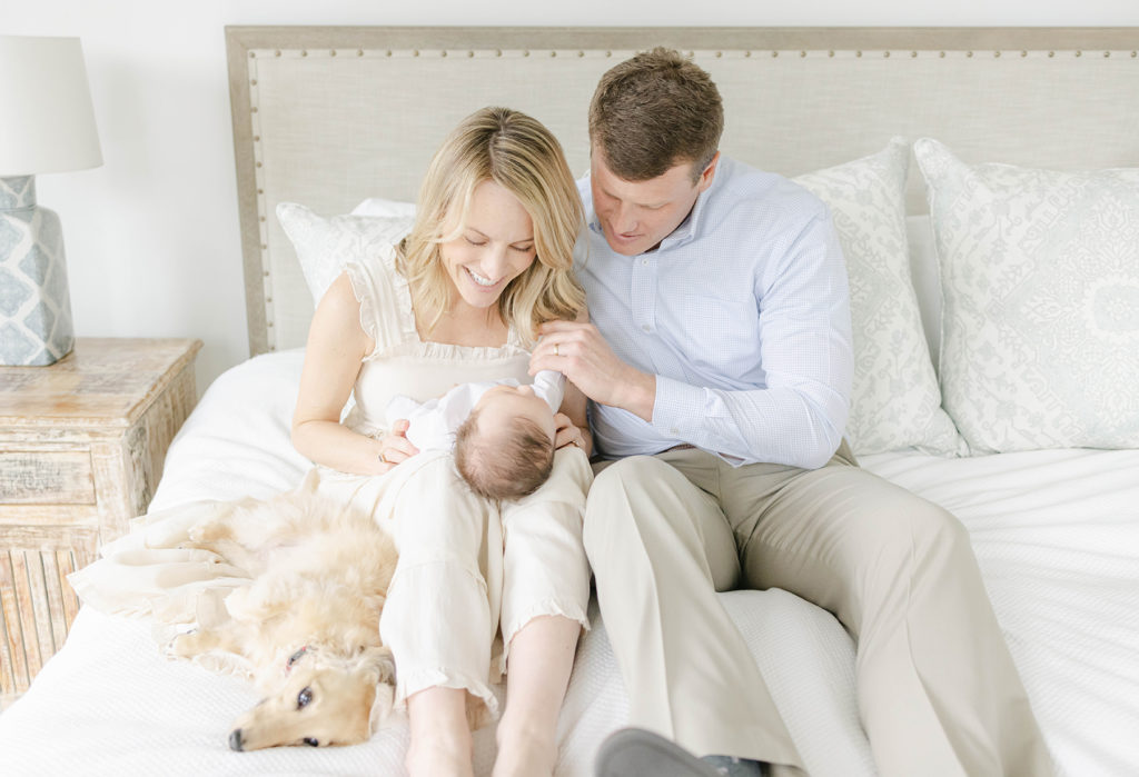 Mom, Dad, and newborn baby on the bed together while dad is holding the baby's hand by Mountain Brook newborn photographer 