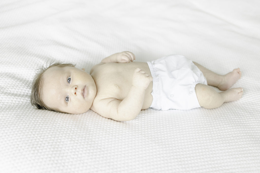 Newborn baby boy lying on white bedding wearing bloomers by Birmingham newborn photographer