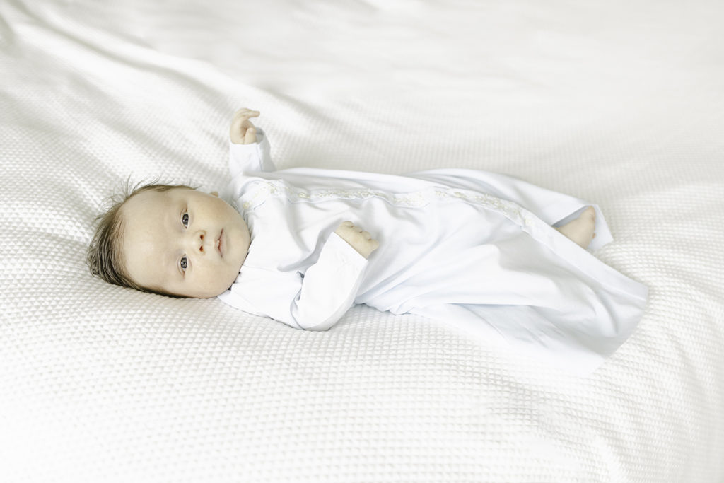 Newborn baby wearing daygown lying on white bedding by Birmingham newborn photographer