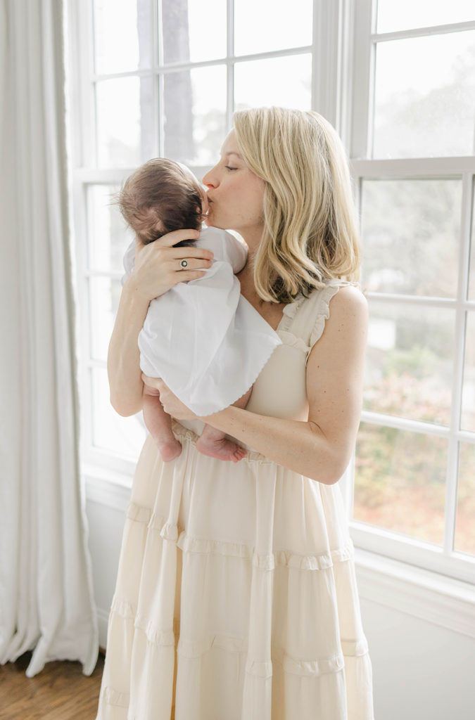 Mom kissing newborn baby boy standing in front of a window by Mountain Brook newborn photographer 