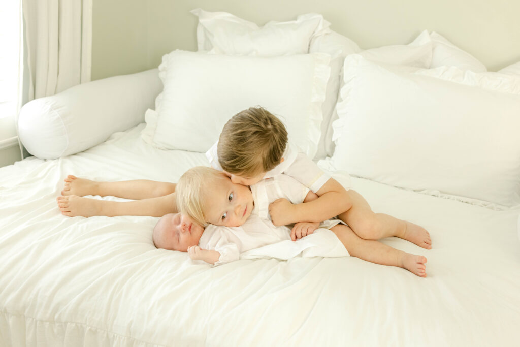 3 brothers lying on bed and loving on newborn baby by Birmingham Newborn Photographer