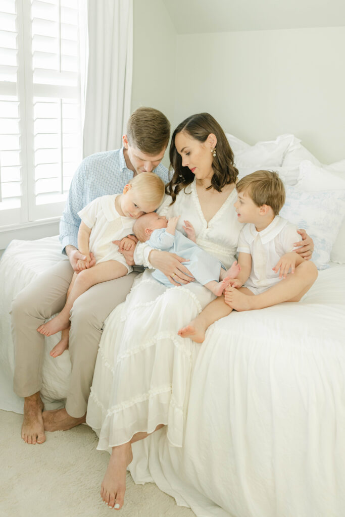 Family of 5 sitting on bed loving on newborn baby by Birmingham Newborn Photographer