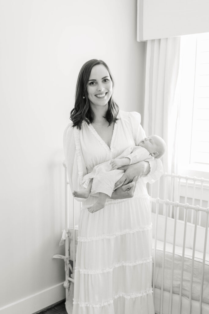 Mom holding newborn baby in front of crib by Birmingham Newborn Photographer