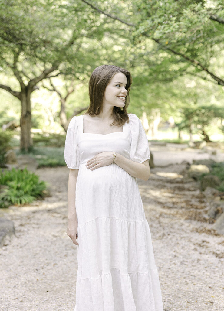 Mom holding hand on top of baby bump and smiling off into the distance by Birmingham Maternity Photographer 