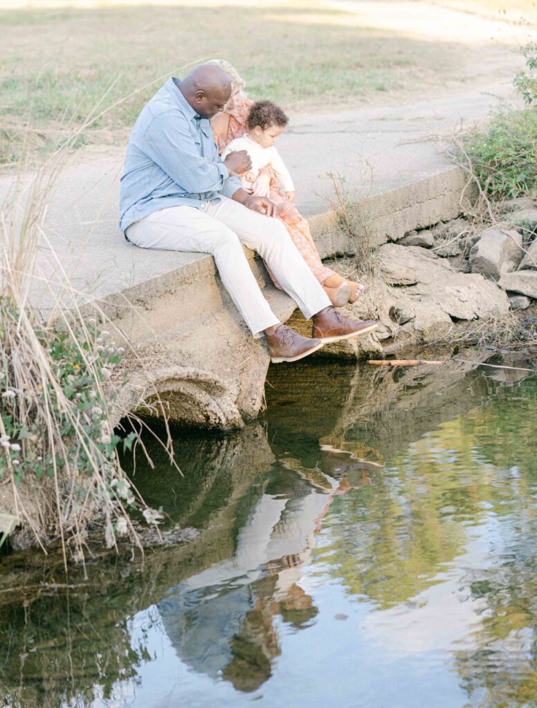 Family of 3 sitting on a bridge looking down into the water by Birmingham Lifestyle Photographer - Whitney Carr 