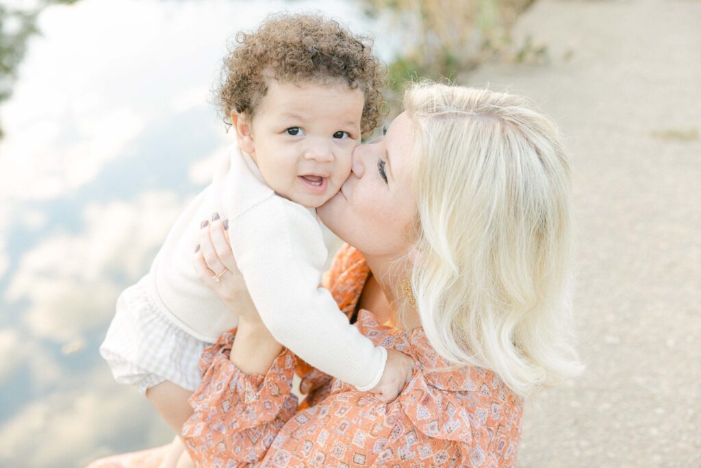 Mom kissing Baby's cheek while he looks at the camera, lifestyle family photography - Whitney Carr Photography