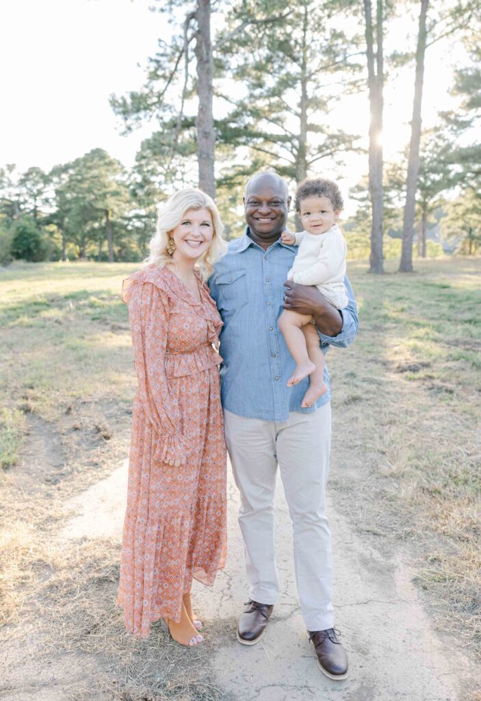 Family of 3 standing in a field smiling at the camera  - Whitney Carr Photography