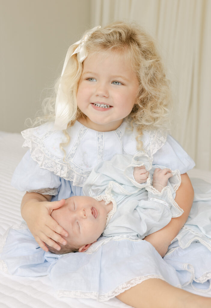 Older sister holding newborn baby brother by lifestyle newborn photographer